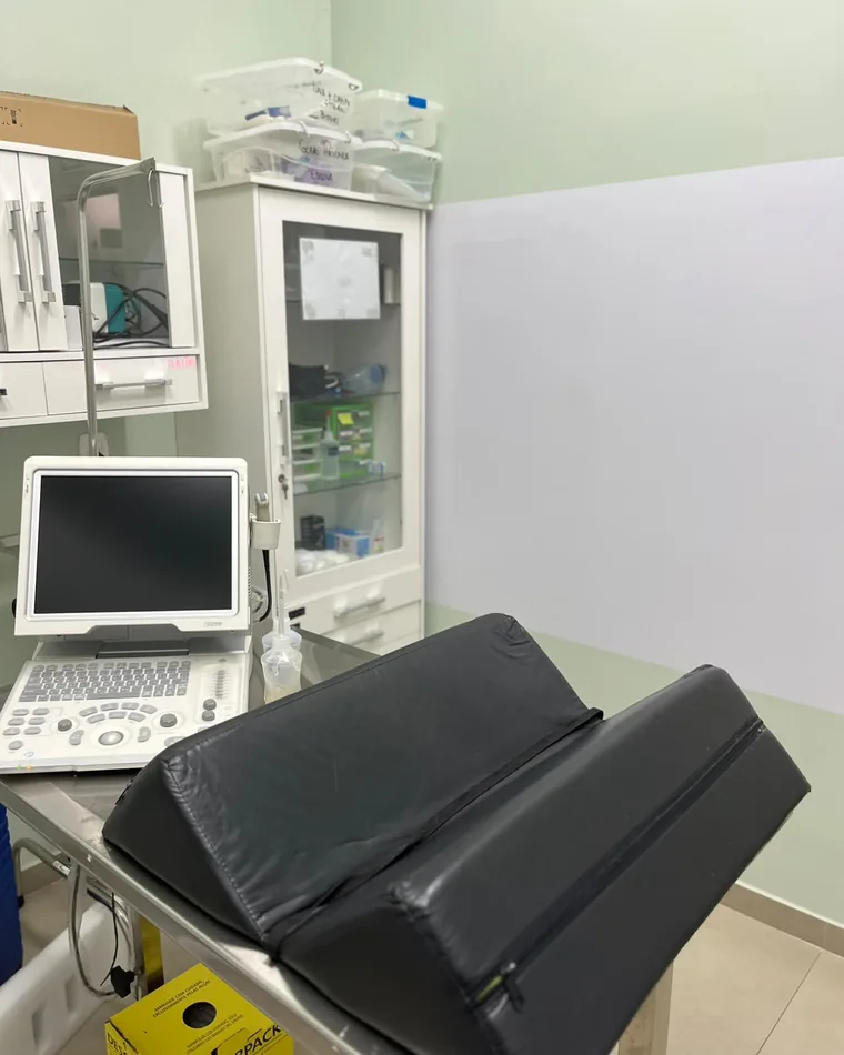 Sala de exames com aparelho de ultrassom e mesa acolchoada para o paciente.
